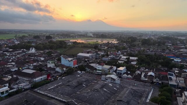 Sunrise panorama of Kepanjen town with rice paddies, mosque dome and distant volcano silhouette.