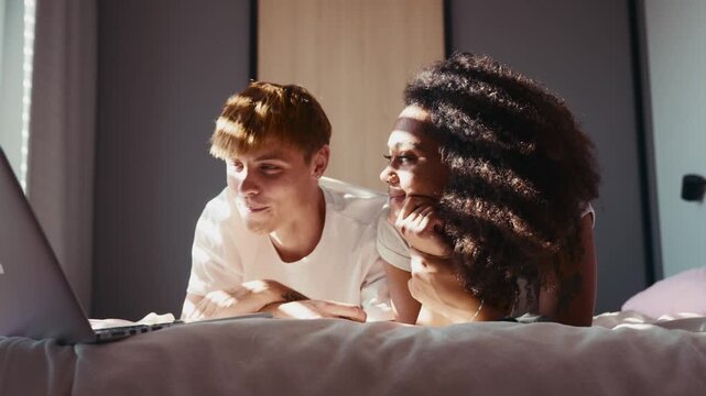 Modern couple enjoying streaming entertainment, lying in bed.