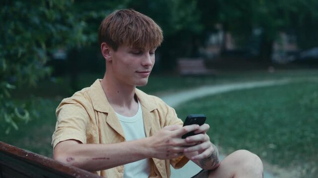 Male college student starting new academic year, waiting for friends in park.
