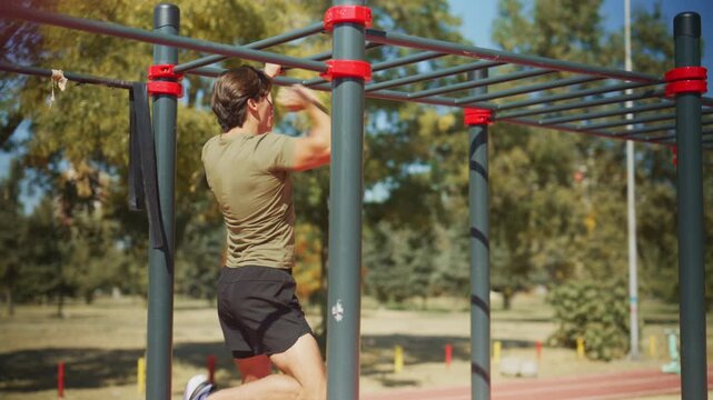 Man performs a monkey bar workout at an outdoor calisthenics park, moving hand over hand to build upper body strength.
