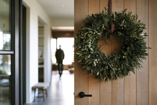 A beautiful wreath hangs on a door, leading to a warm, inviting interior, symbolizing hospitality and the essence of home during the festive seasons.