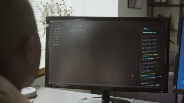 African American man typing programming code on keyboard viewed over shoulder at computer monitor. Clip fits software development, IT tutorials, and tech promos