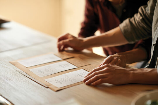 Two individuals thoughtfully discussing their meal choices while browsing menus on a stylish wooden table, highlighting the essence of dining out and culinary exploration together.