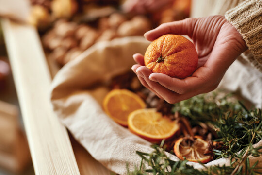 A hand holding a vibrant orange above a collection of dried fruits and herbs, emphasizing the contrast and beauty of fresh and preserved foods set in a colorful display.