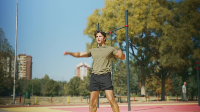 Athletic man warms up with high knees, elbow strikes and arm swings during an outdoor fitness workout at a calisthenics park.