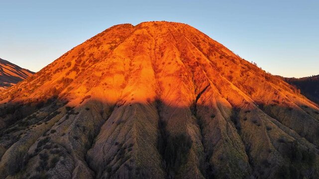 Sun glows warmly over rugged Mount Batok peak. Golden light paints slopes with rich, earthy tones
