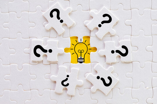 White jigsaw puzzle pieces with question marks surrounding a yellow lightbulb icon. Concept of problem solving, finding solutions, creative idea generation, and business innovation.