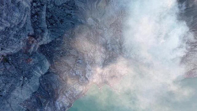 Topdown drone view of Mount Ijen crater with steaming fumaroles and turquoise acidic lake.