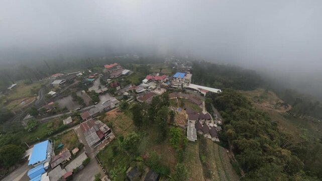 Foggy aerial fisheye view of mountain village, terraced farms and winding roads.