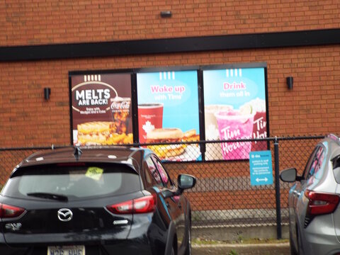 Gloucester, Ontario, Canada &ndash; August 04, 2025: Three "Tim Hortons food and drink advertisement panels" hang on a red brick wall behind a chain-link fence on Montr&eacute;al Rd.