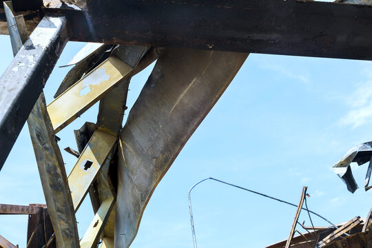 Scraps of metal frame, debris are visible under heavy tornado in worksite with broken structures.