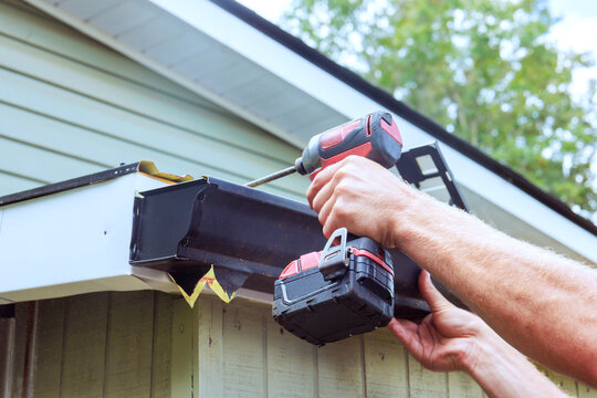 Builder works on installing gutter using power drill at house