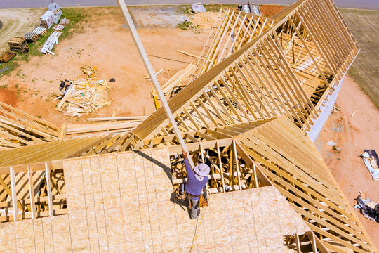 Construction worker uses long beams pole to help with roofing on building under construction