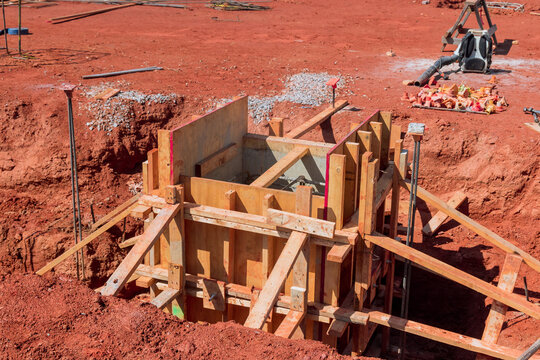Workers set up wooden structure in hole at construction site. concrete foundation work