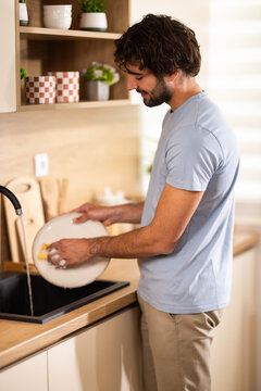Young man washing dishes in modern kitchen with natural light