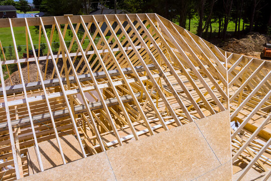 Workers are constructing building with wooden roofing frame, surrounded by trees