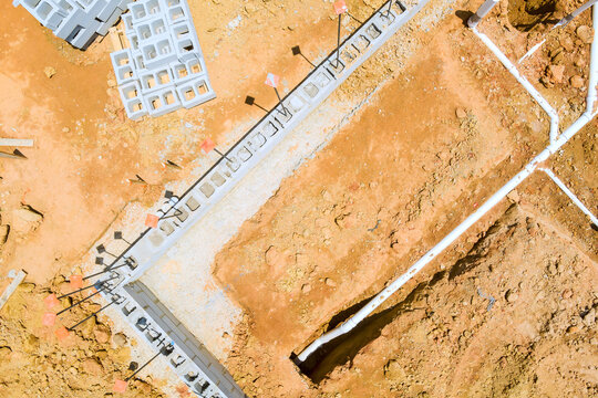 Workers are pouring concrete for foundation while machinery moves earth at building site in city.