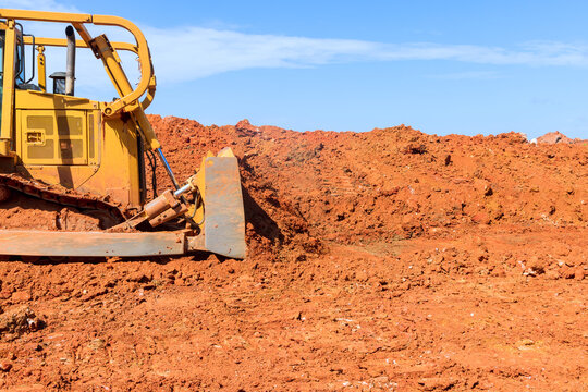 Large excavator shifts red dirt at construction site under earth moving