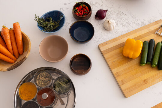 Cutting board is holding yellow bell pepper and green zucchinis on marble counter with spice box
