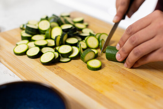 African American man slicing zucchini with chef's knife on cutting board on counter with blue bowl
