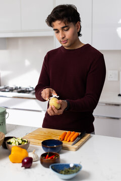 Adult African American man peeling potato with peeler at kitchen counter in maroon sweater