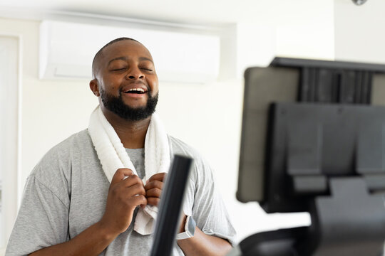 Mature African American man resting, catching breath in home gym with towel and smartwatch