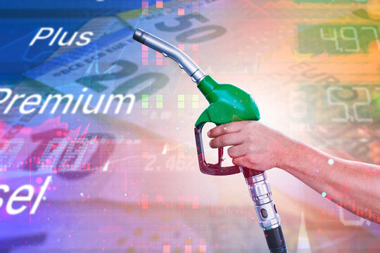 Hand holding a green fuel nozzle with gasoline price displays and financial market charts in the background. Fuel costs, energy prices and oil market trends concept for automotive advertising.