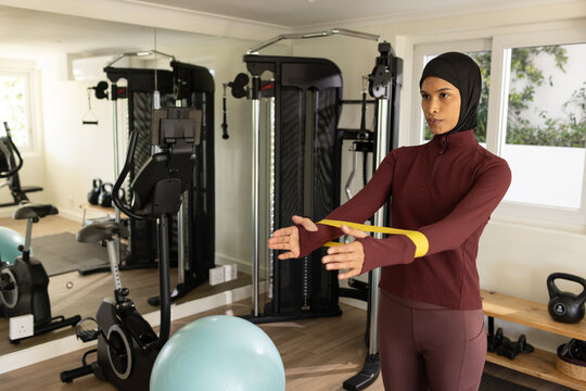 African American woman using yellow loop band in home gym wearing maroon athletic wear, copy space