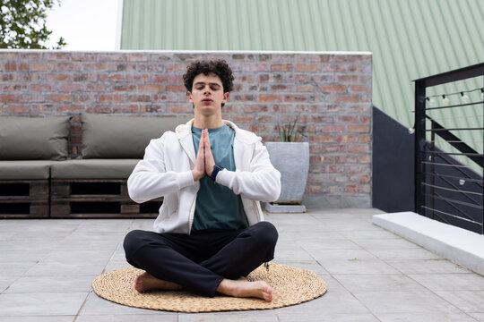 Man sitting cross-legged meditating on tiled rooftop terrace on woven mat, wearing smartwatch