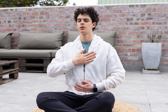 African American man meditating on mat on rooftop, wearing hoodie, smartwatch near pallet table