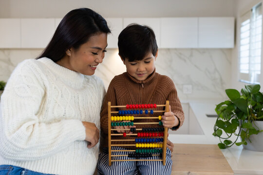 Mother and child son wearing sweaters leaning in, son manipulating abacus on kitchen countertop
