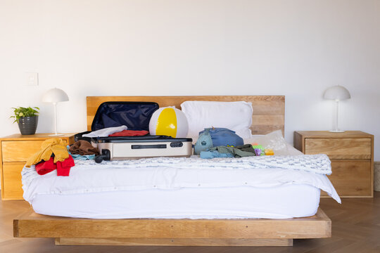 Wooden platform bed is holding open suitcase with folded clothes and beach ball in bedroom