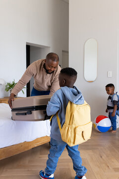 African man with two African boys placing beige suitcase on bed in bedroom with yellow backpack