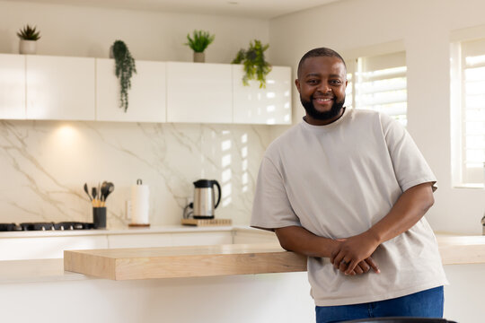 Adult African man leaning on wood island in modern kitchen smiling with stovetop kettle, copy space