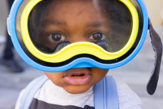 African American boy wearing blue-yellow snorkel blue straps gray shirt facing camera near steps