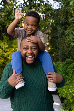 African father and son smiling, father carrying son on shoulders in backyard, showing wedding ring