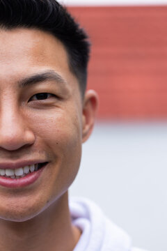 Asian man smiling while wearing white hoodie by red horizontal banded wall, copy space