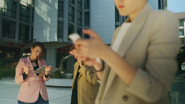 Business people actively engage in various tasks with their digital devices in a modern urban environment. They are seen communicating on phones and working with tablets outdoors on a sunny day.