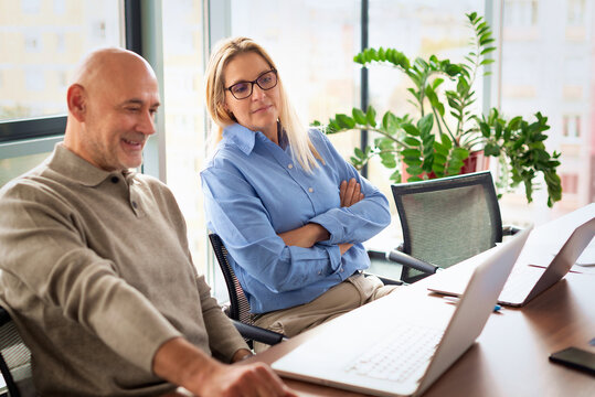 Mature businessman and female colleague collaborating on a laptop in a modern office conference room