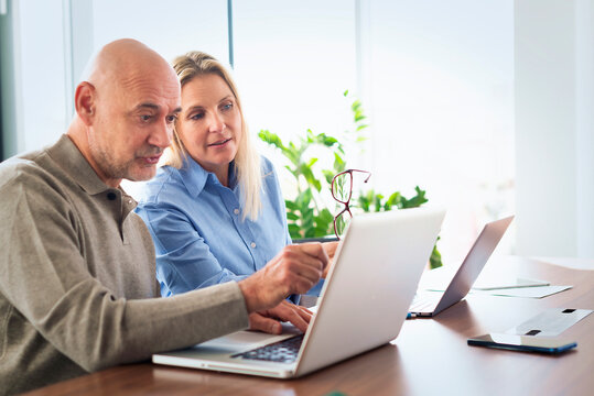 Mature businessman and female colleague collaborating on a laptop in a modern office conference room