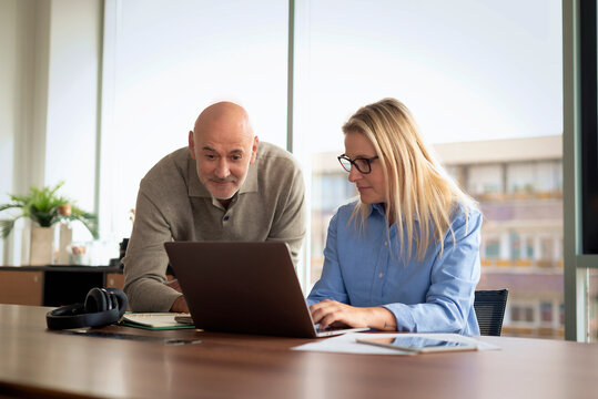 Mature businessman and female colleague collaborating on a laptop in a modern office conference room