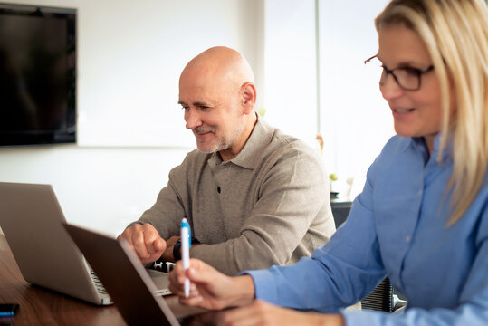 Mature businessman and female colleague collaborating on a laptop in a modern office conference room