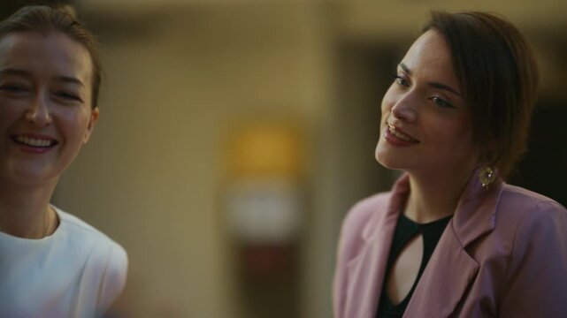 A confident businesswoman in a pink blazer smiles and laughs during a lively conversation with colleagues.