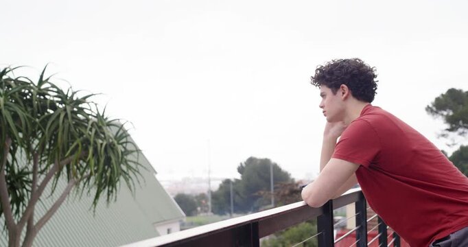 African American man leaning on balcony rail, resting chin on watch, scanning far view, reflecting