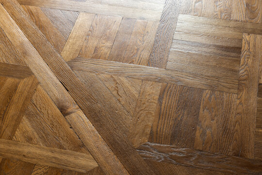 Wooden parquet floor displays a geometric pattern and detailed wood grain texture indoors. Warm natural tones and soft highlights create a classic surface for interior design, architecture, flooring