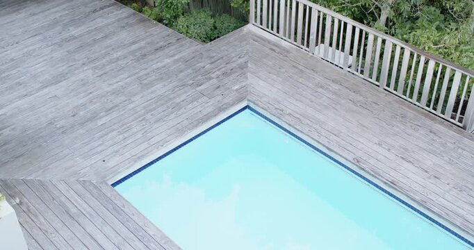 Camera is pulling back and tilting upward to reveal backyard pool corner, deck, railing, shrubs
