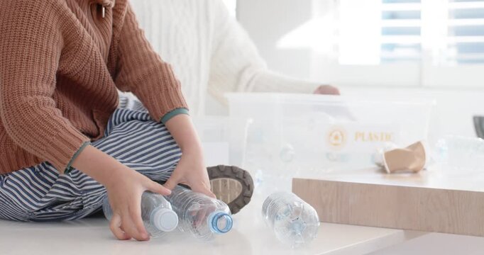 Asian mother and son playing with bottles in kitchen, holding PLASTIC bin and recycling bottles