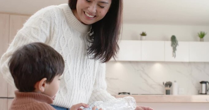 Asian mother and child son leaning, guiding sorting plastic bottles into marked bins on glass table