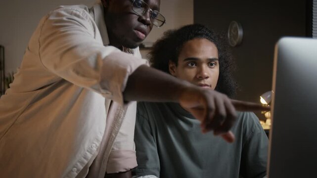 African American mentor pointing at desktop computer screen while assisting young colleague in office, tilt up view. Footage ideal for software development and IT training campaigns