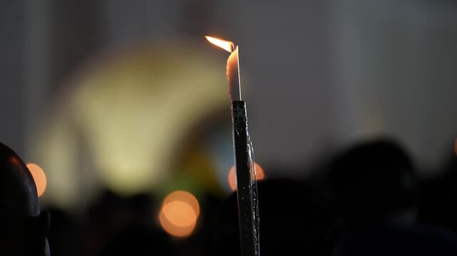 Ground-level slow motion closeup of a burning candle held during St Anne festival procession.
